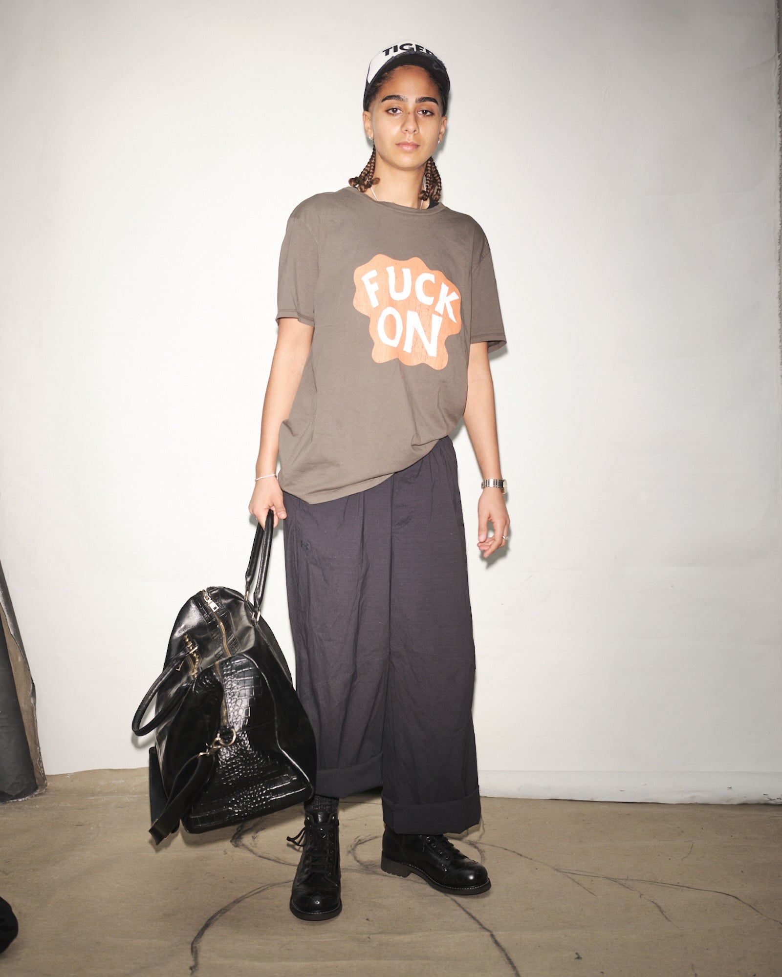 Person wearing a graphic t-shirt with text, holding a black bag against a plain background