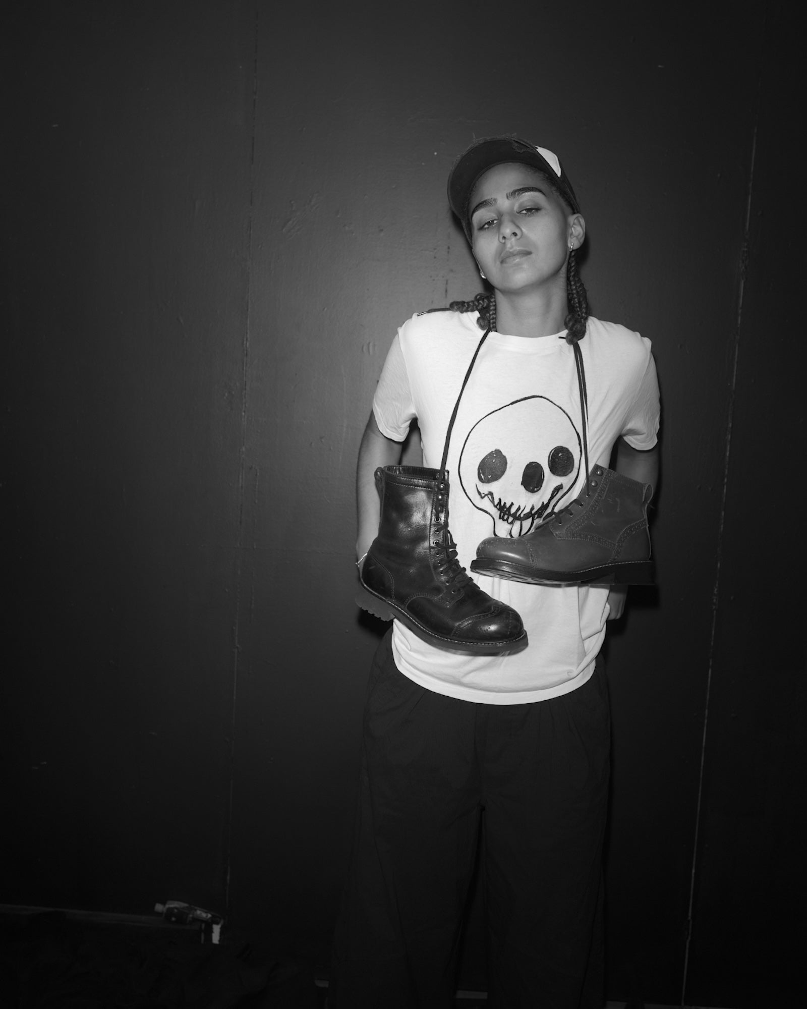 Amani Smith holding two Bum Society boots in a Waldersten x Bum Society t-shirt against a dark background