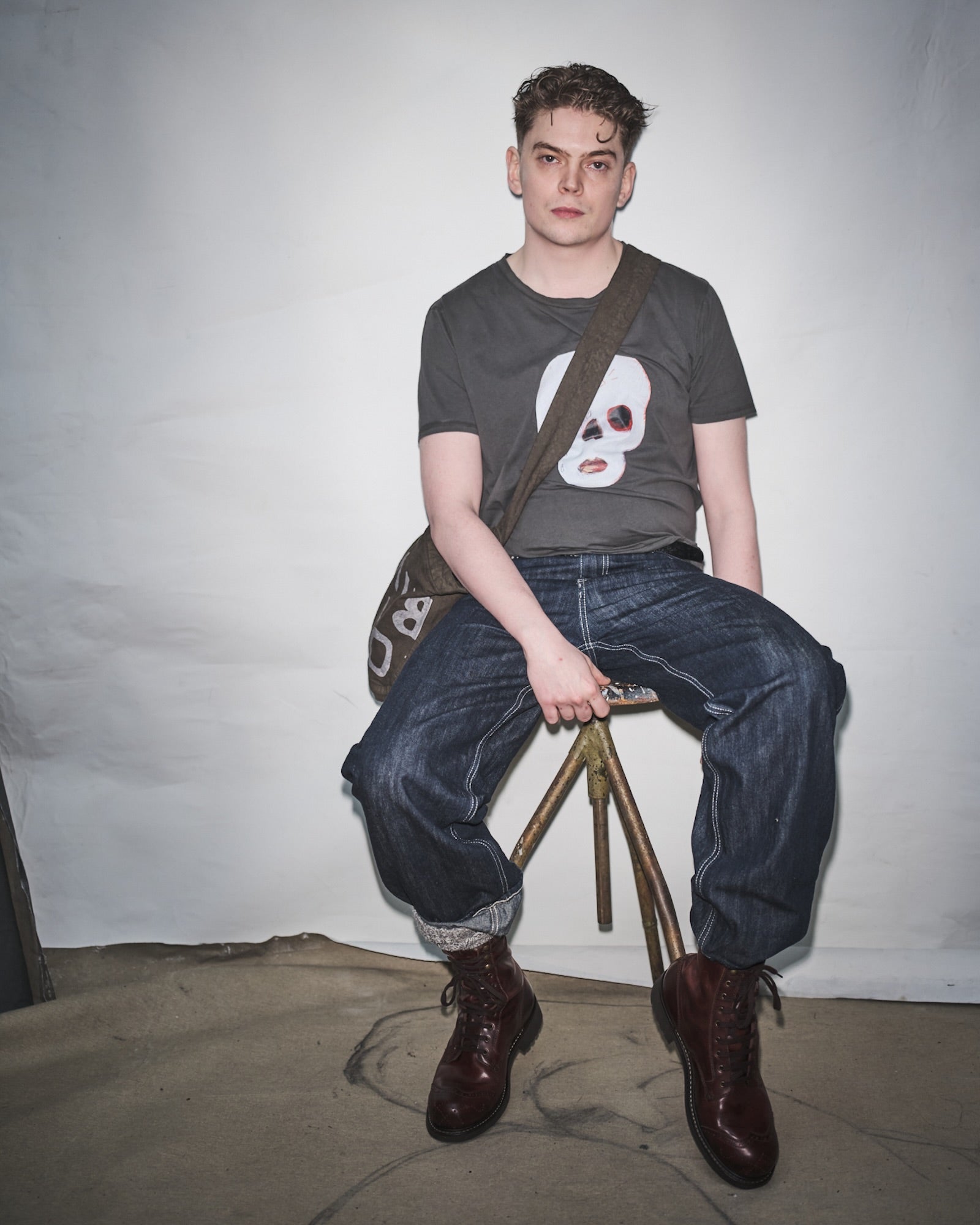 Bertil Kugelberg sitting on a stool wearing a Waldersten x Bum Society t-shirt, Bum Society boots and jeans against a plain background