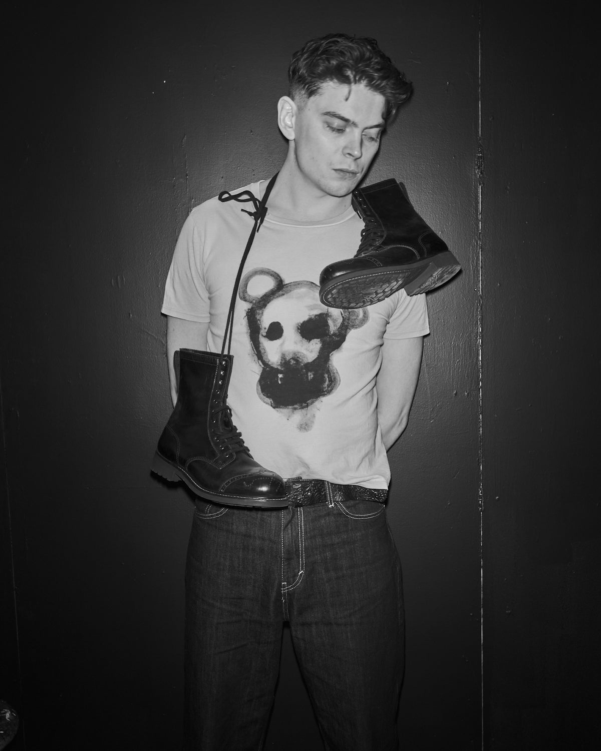 Bertil Kugelberg with boots hanging around the back of the neck a Waldersten x Bum Society t-shirt with on a dark background