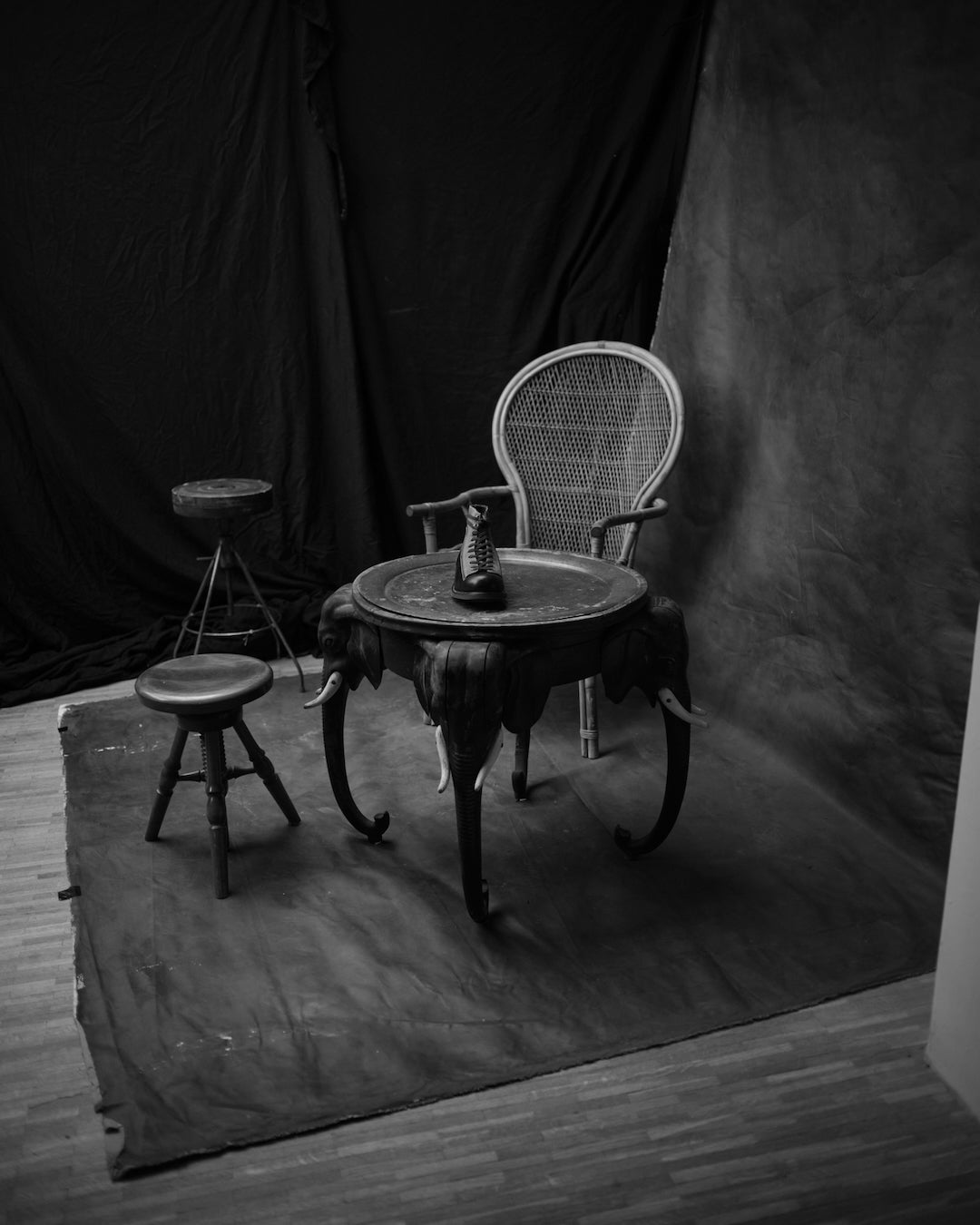Black and white photo of a chair Bum Society boots on table and stool against a dark backdrop