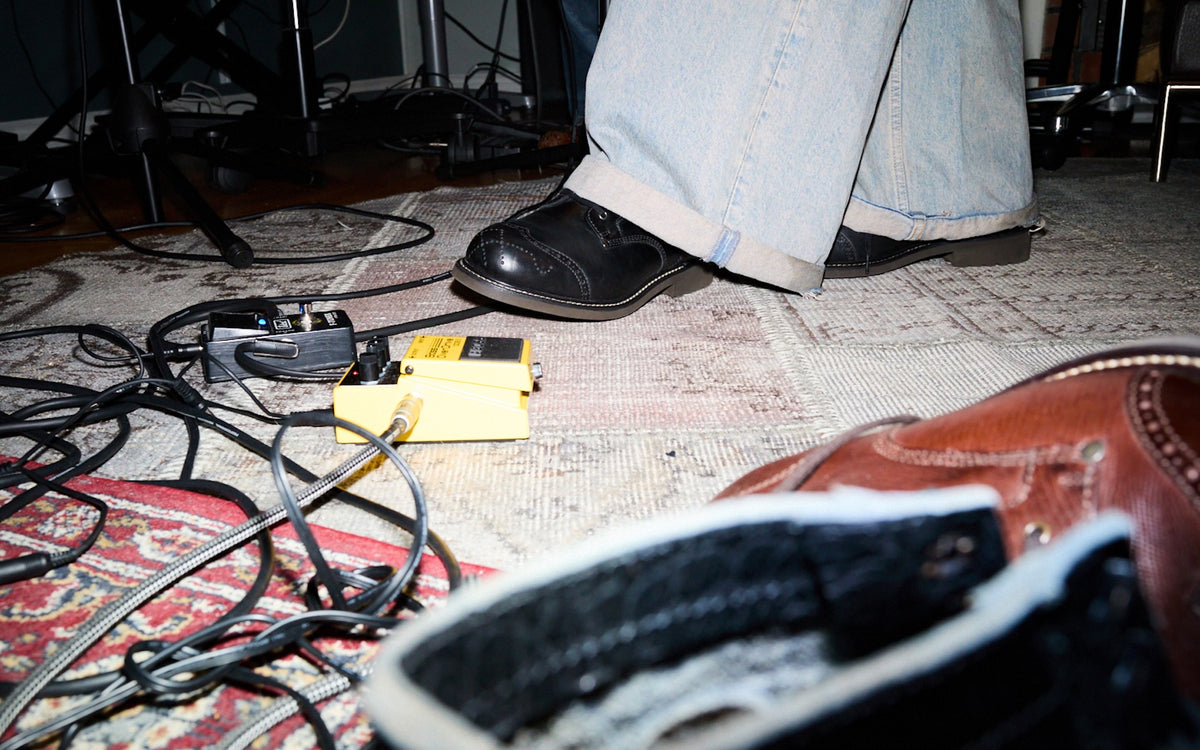 Close up person wearing Bum Society boots with guitar pedals and cables on studio floor