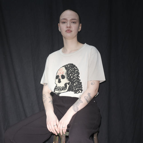 Person wearing a Waldersten x Bum Society original artwork Lady Dead for Waldersten x Bum Society collaboration on a stool against a black background color:mud