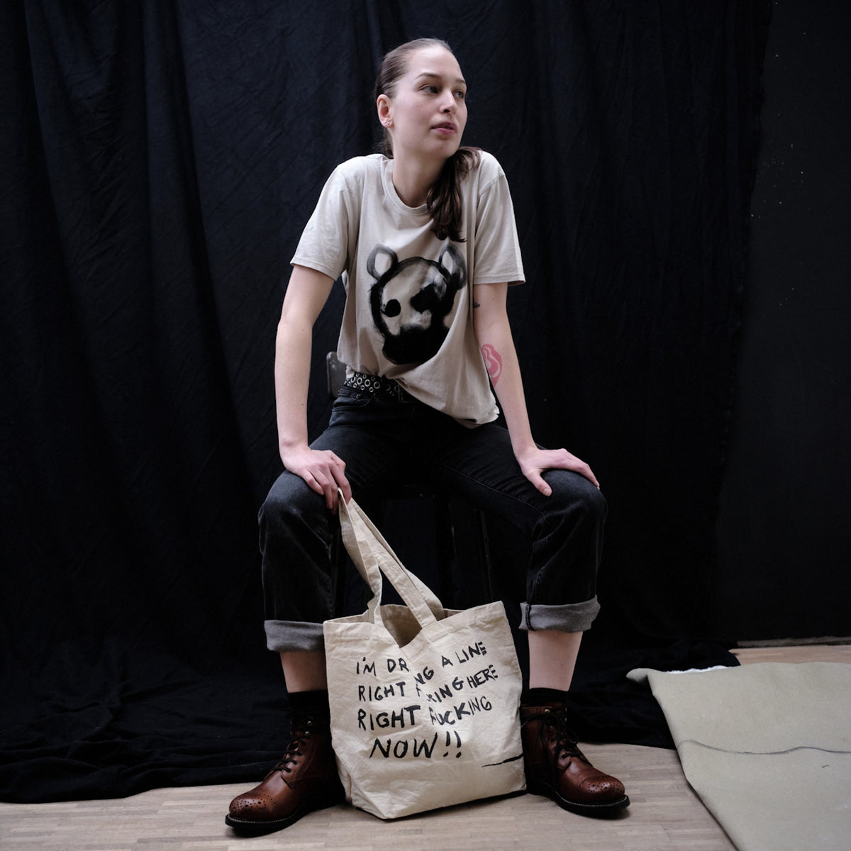 Person sitting against dark background in an original artwork t-shirt by Waldersten x Bum Society namned Animal Boy color:mud