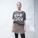Person wearing a Bum Society reversed logo t-shirt  and a brown skirt against a white background color:ink