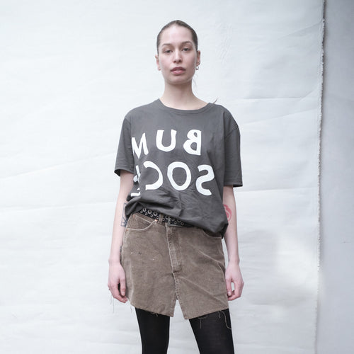 Person wearing a Bum Society reversed logo t-shirt  and a brown skirt against a white background color:ink