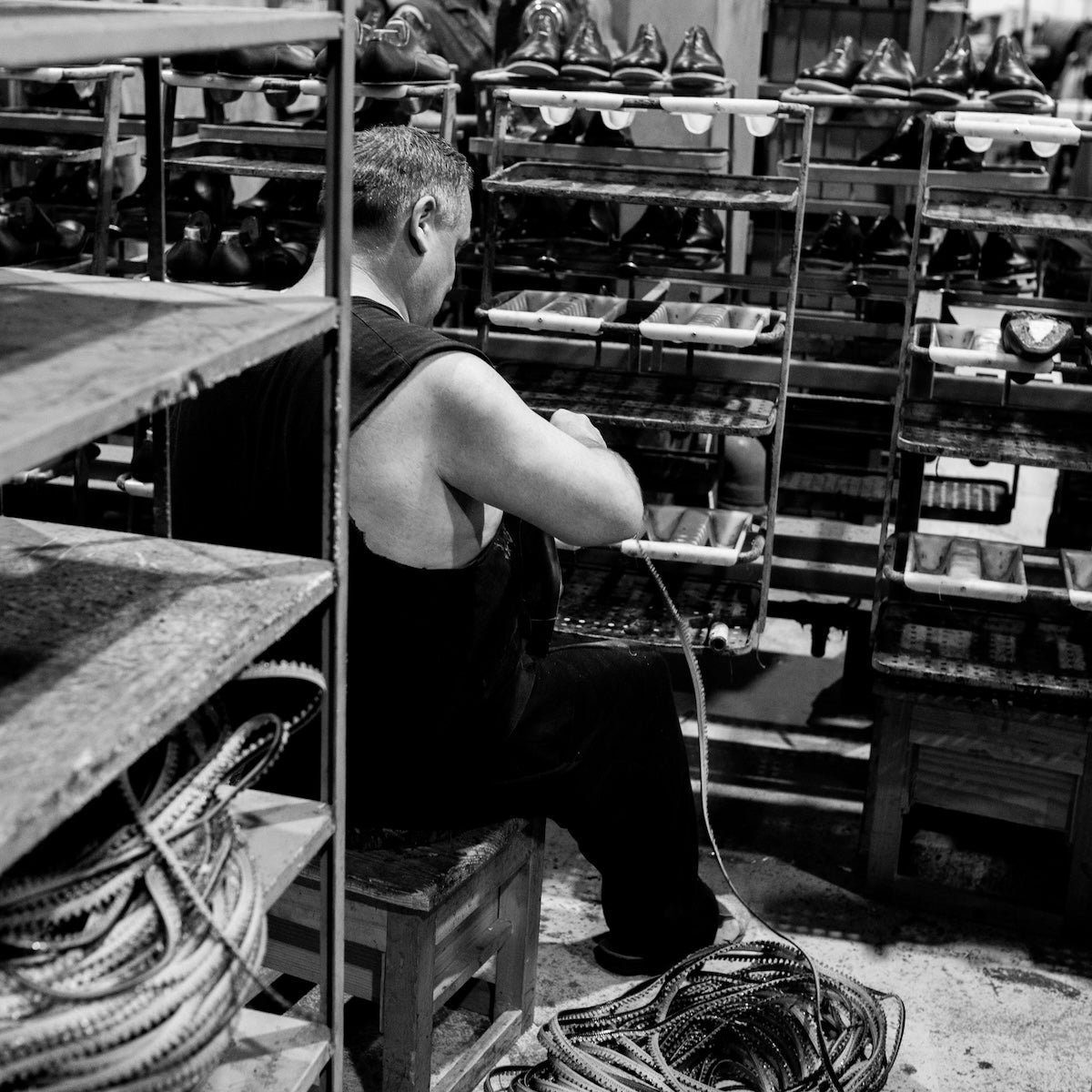 Man organizing welt sitting among shelves filled with shoes in a factory setting
