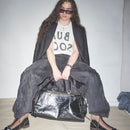 Person wearing a black outfit with sunglasses, holding Bum Society leather duffle bag color:shiny black,snow