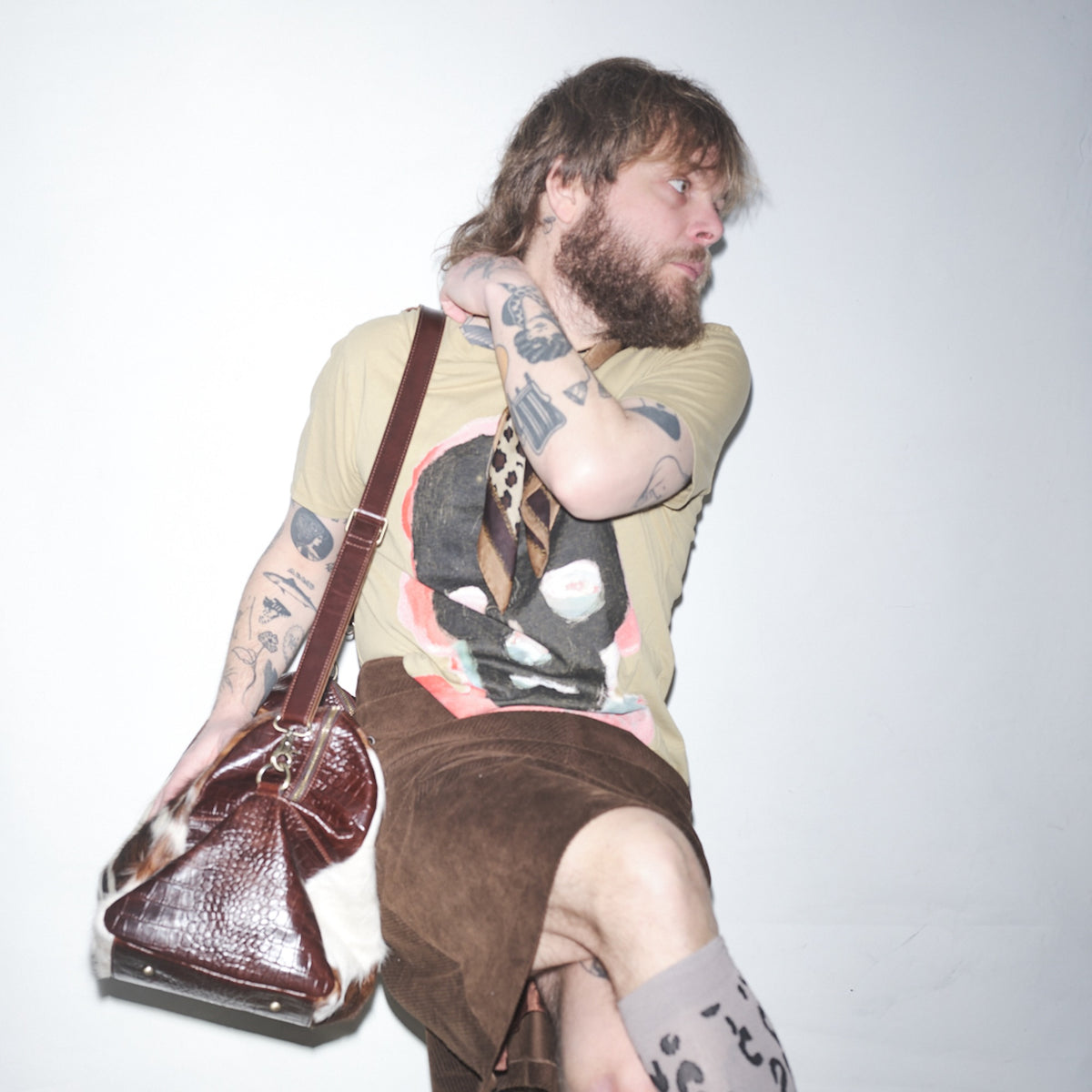 Person with tattoos holding a Bum Society pony hair duffle bag in a Waldersten x Bum Society t-shirt namned Exray against a plain background color:dandy brown,earth