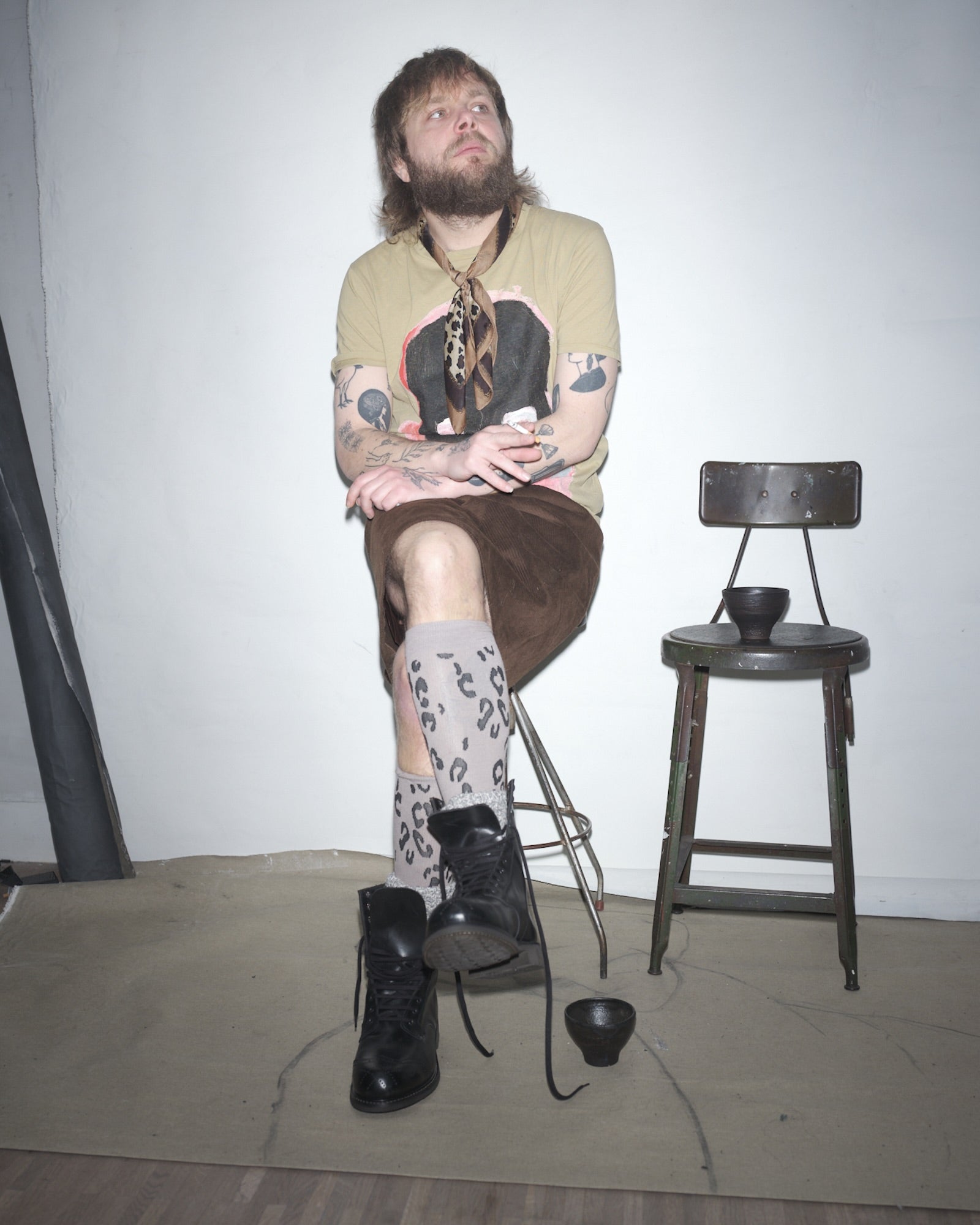 Johnny Ahr sitting on a chair with tattoos and a beard, wearing a Waldersten x Bum Society t-shirt and black Bum Society boots.