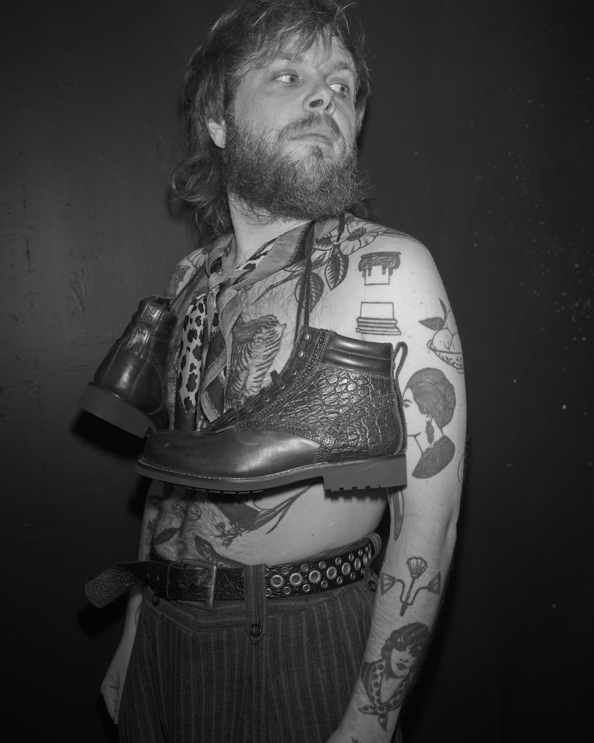 Johnny Ahr with tattoos holding Bum Society boots against a dark background