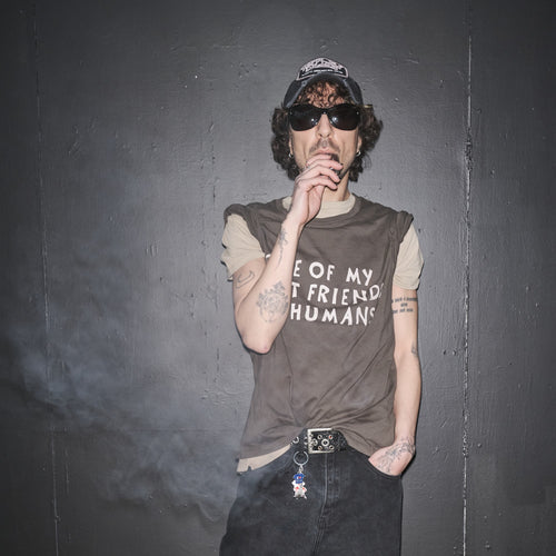 Person wearing a Some Of My Best Friends Are Human t-shirt by Bum Society with sunglasses, and a cap against a dark background color:ink