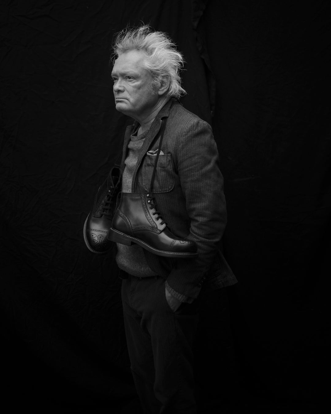 Dark black and white portrait Claes Bondelid in studio with boots hanging around neck