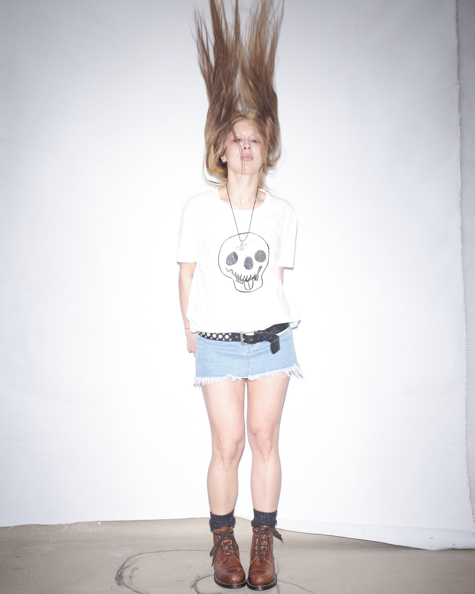 Nena Vadman wearing a white Waldersten x Bum Society t-shirt with art work, denim shorts, and brown Bum Society boots on a plain background.