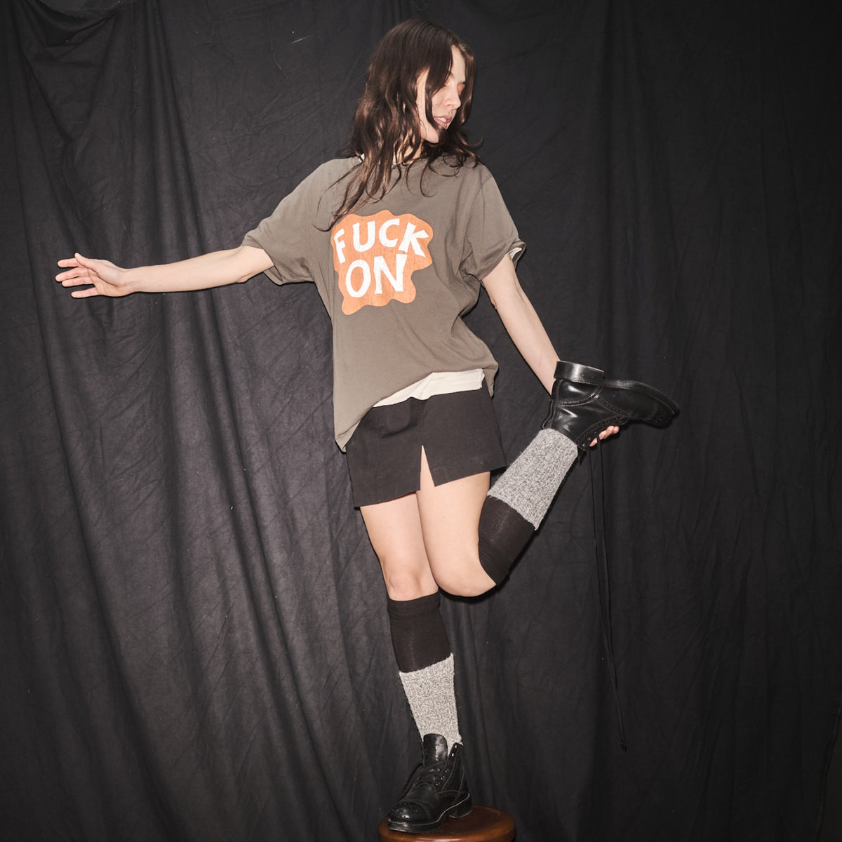 Person wearing a Fuck On, Ongoing t-shirt  t-shirt by Bum Society standing on stool against a black curtain color:ink