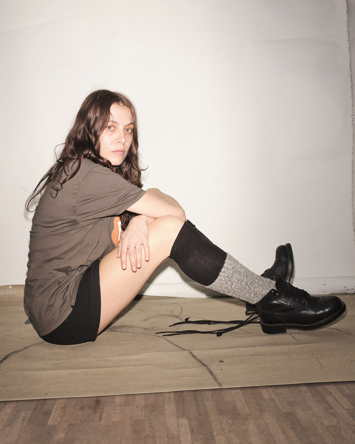 Olivia Henriksson sitting on the floor wearing an ink t-shirt, black shorts, and black Bum Society boots with gray socks.