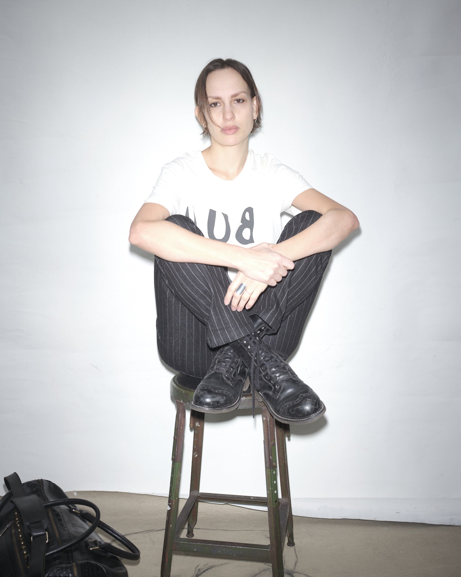 Rakel Lindgren sitting on a stool wearing a Bum Society t-shirt and black Bum Society boots against a plain background