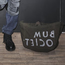 An almost black canvas tote bag with logo print in white letters, shown next to a person's leg wearing a black boot.