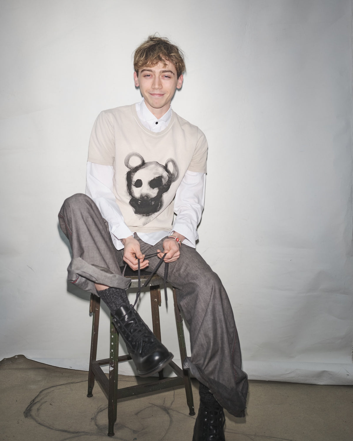Vanja Filipovic sitting on a stool wearing a sweater with a Waldersten x Bum Society art work, gray pants, and black Bum Society boots.