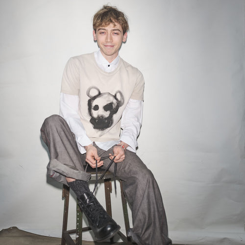 Person wearing an original Waldersten x Bum Society t-shirt Animal Boy artwork sitting on a stool against a plain background color:mud