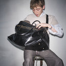 Person holding a Bum Society leather duffle bag Shiny Black against a plain background color:shiny black