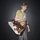 Person holding a pony hair Bum Society duffle bag Dandy Brown against a dark background color:dandy brown 